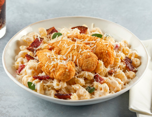 Mac and cheese topped with chicken tenders, bacon, Parmesan, and sliced scallions in a white bowl