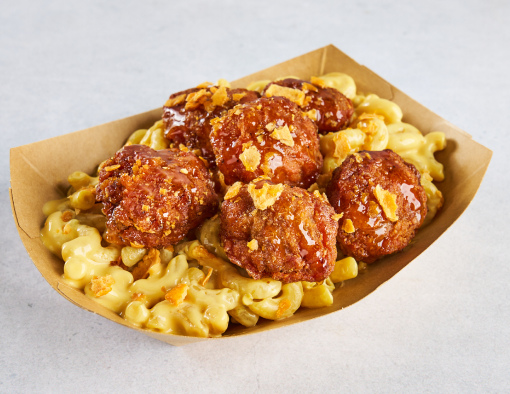 A paper to-go container with breaded beef bites sitting atop mac & cheese  