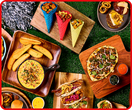 An assortment of game day appetizers including tacos, spicy cheese dip, wings and pizza on a table