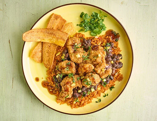A plate of fried chicken over rice and beans with fried plantains and cilantro