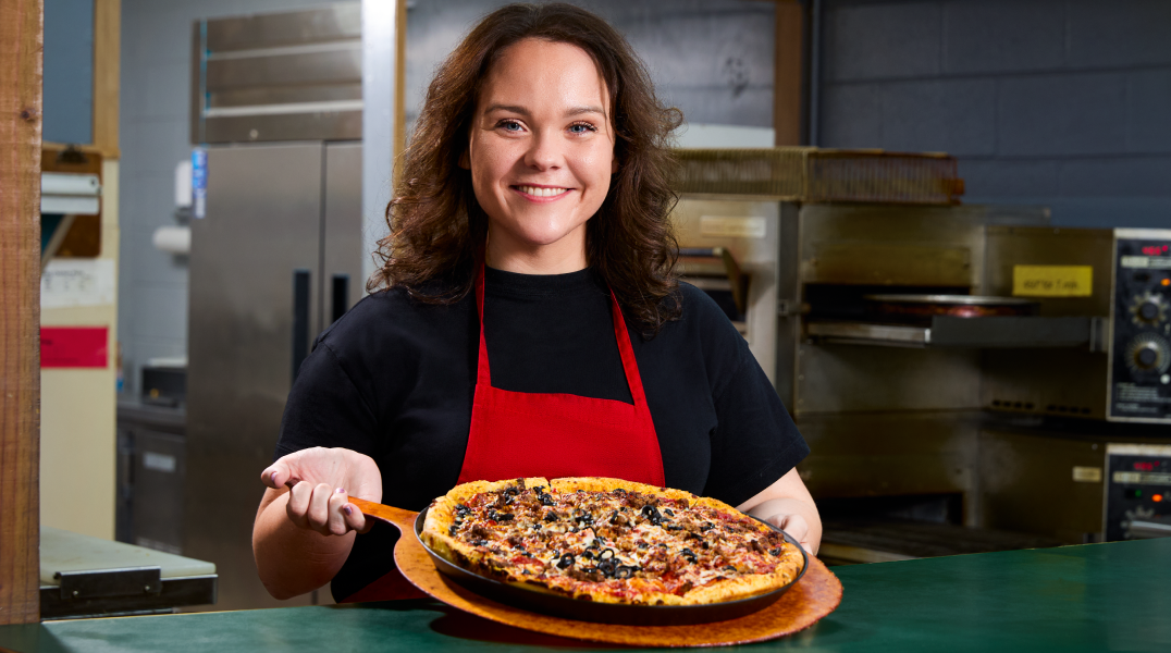 2024 Great Pizza Give Back Winner, woman in red apron holding a pizza
