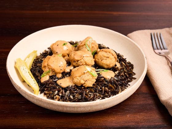 Cajun beef bites with Creole gravy on wild rice, garnished with pickled okra and parsley in a white bowl