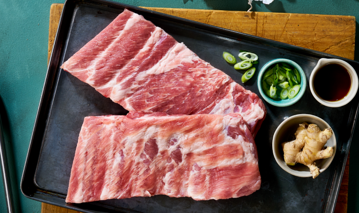 Raw rack of St. Louis-style pork ribs on metal prep tray